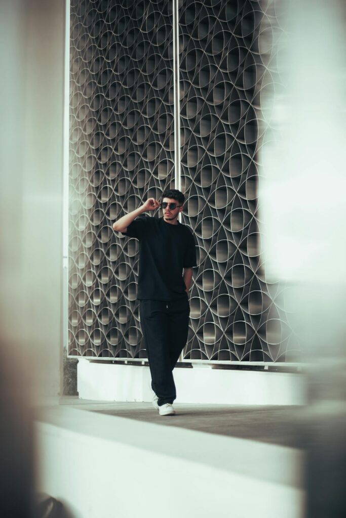 Stylish man in casual black outfit and sunglasses posing outdoors, representing modern gents wear fashion.