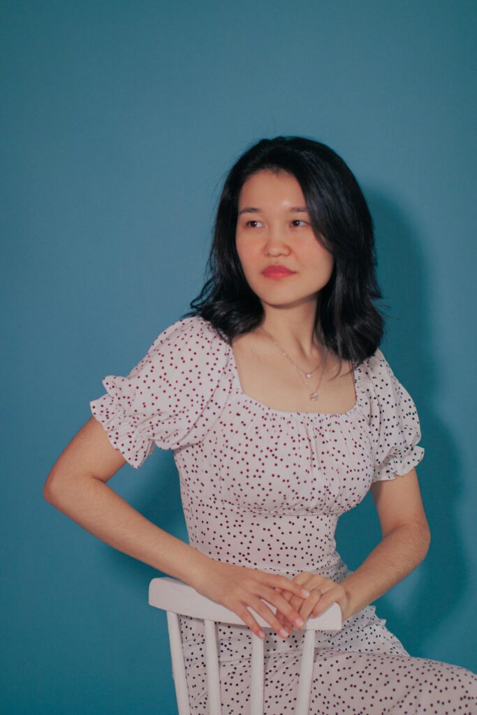 Woman wearing a stylish white polka dot dress sitting on a chair against a blue background, representing modern ladies wear fashion.