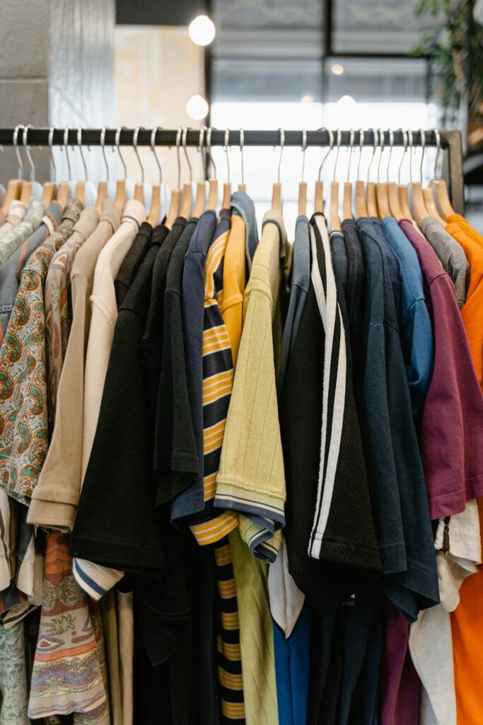 Stylish men's and women's shirts on wooden hangers displayed on a boutique clothing rack, featuring striped, paisley, and solid color designs in a well-lit fashion store interior