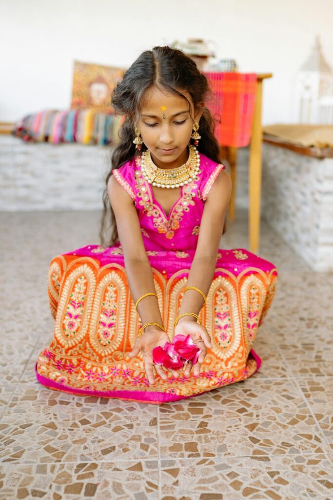oung girl dressed in a colorful traditional outfit holding flower petals, showcasing festive kids wear fashion.